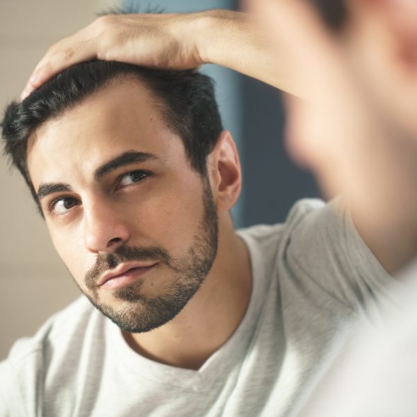 Man Worried For Alopecia Checking Hair For Loss Latino person with beard grooming in bathroom at home. White metrosexual man worried for hair loss and looking at mirror his receding hairline.